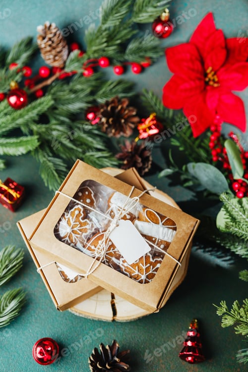 Preview: Gingerbread cookies in gift box with festive greenery and red ornaments on dark background