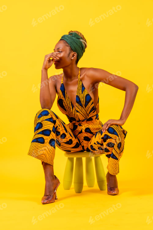 Preview: Young African woman in traditional dress on yellow background, sitting, commercial photography