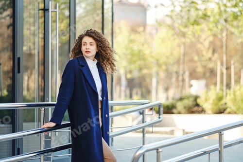 Preview: Young woman in wool coat posing near modern building