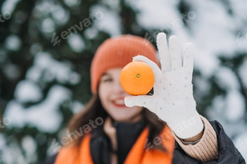 Preview: Close-up of woman holding an orange in a snowy outdoor scene. Winter immunity, fresh citrus