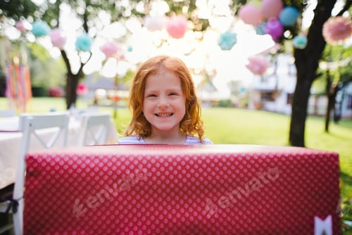 Preview: Portrait of small girl with present outdoors in garden in summer.