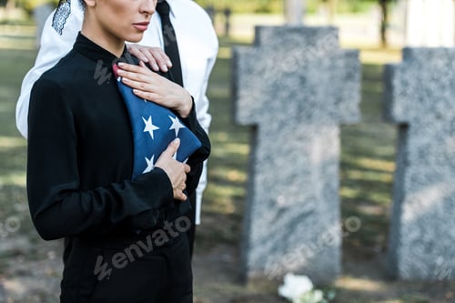 Preview: cropped view of senior man near woman with american flag on funeral