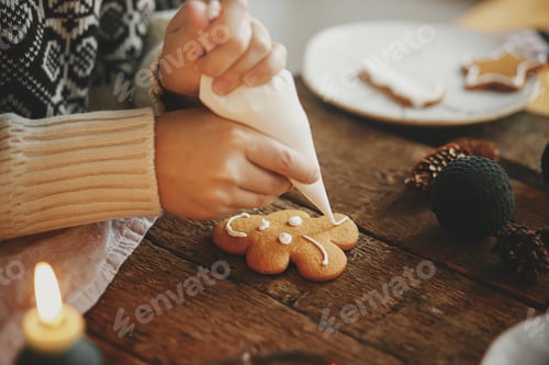 Preview: Hands decorating christmas gingerbread cookie reindeer with icing on rustic table. Making cookies