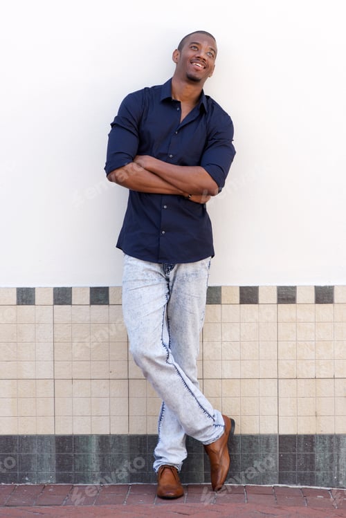 Preview: young black man smiling against white wall with arms crossed