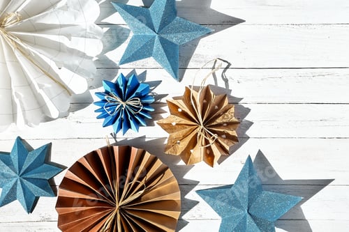 Preview: Paper snowflakes, paper blue stars and fans made of craf paper on white wooden table.