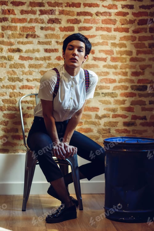 Preview: Beautiful young woman, model of fashion, with very short haircut, looking at camera sitting on chair