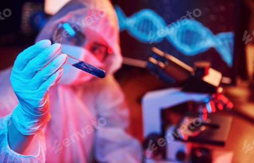 Preview: Nurse in mask and white uniform, holding tube with liquid and sitting in neon lighted laboratory