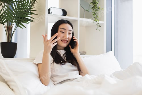 Preview: Asian woman talking on phone while relaxing in bed