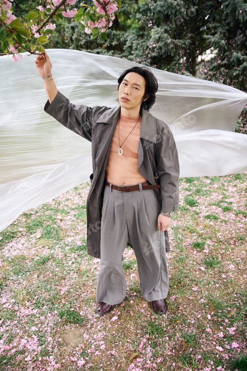 Preview: Stylish young man in grey outfit enjoys a serene park day among blooming flowers