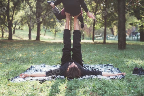 Preview: Healthy young man lying on grass and balancing woman
