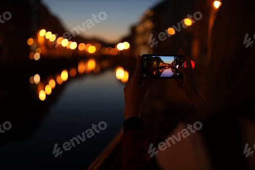 Preview: Hands holding mobile phone and taking photos of night city. Bokeh lights. Tourist.