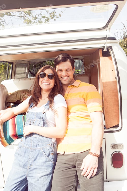 Preview: Couple smiling in front of a vintage camper van on a sunny day.