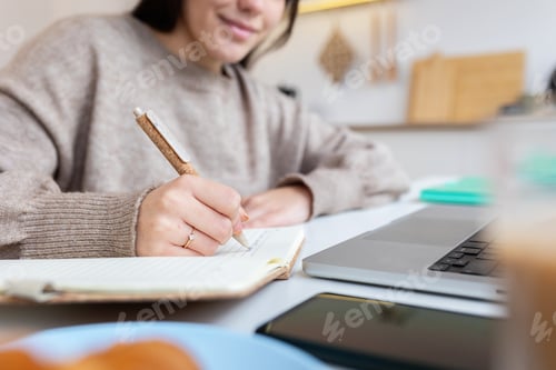 Preview: Teenage student girl writing notes while learning on laptop at home