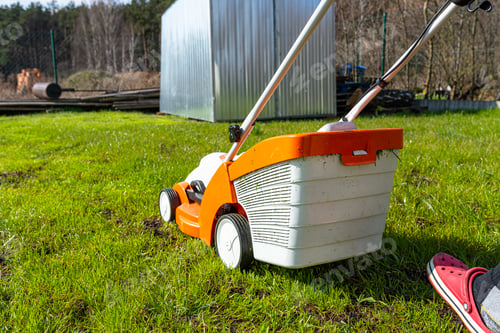 Preview: A man mows the grass with an orange electric mower.