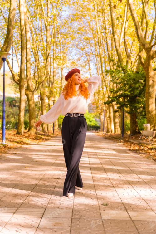 Preview: Red-haired woman in a beret walking through a city forest park at sunset