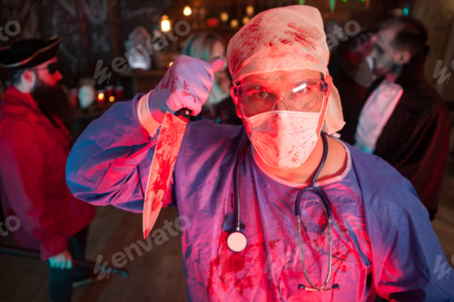 Preview: Attractive young man in a doctor costume holding a knife at halloween party