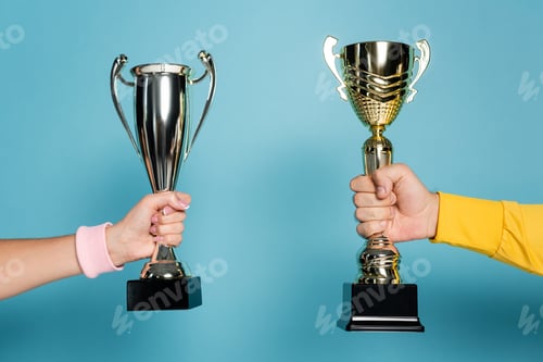 Preview: cropped view of man and woman holding golden and silver trophies on blue
