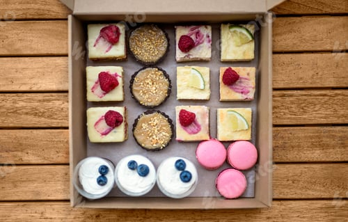 Preview: Selection of colorful and delicious cake desserts in box on table, top view.