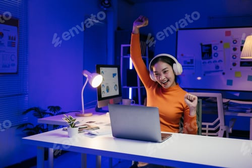 Preview: Excited businesswoman celebrating success working late at night in office