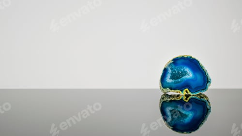 Preview: Blue geode rock crystal with its reflection against a grey background.