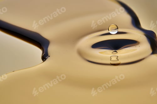 Preview: Texture of cosmetic oil with falling drop on golden background.