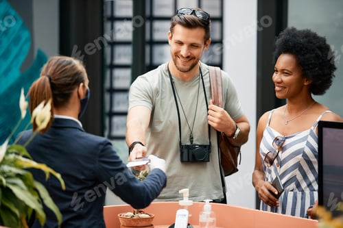 Preview: Happy man and his wife checking in at a hotel while traveling during COVID-19 pandemic.