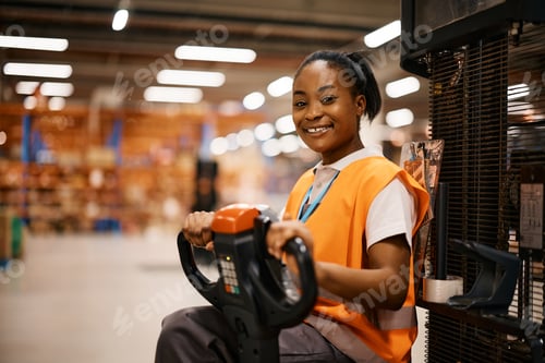Preview: Happy African American woman driving pallet jack while working at distribution warehouse.