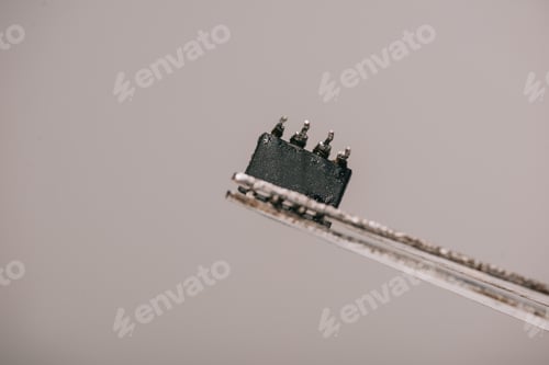 Preview: close up of metallic tweezers with small microchip on grey background