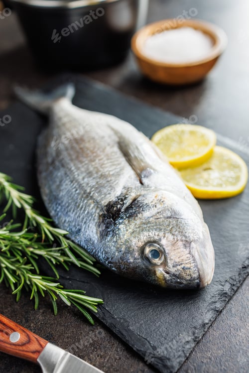Preview: Fresh sea bream fish on cutting board on kitchen table.