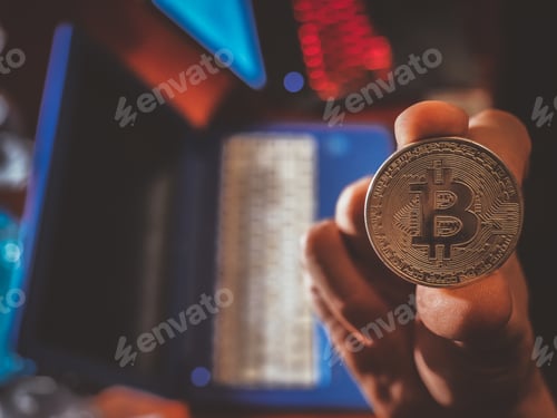 Preview: Closeup of a person holding a bitcoin with laptops on the blurry background