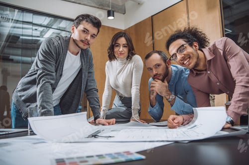 Preview: group of successful architects discussing plans and looking at camera at office