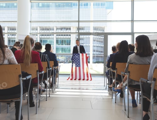 Preview: Male speaker speaks in a business seminar in office building with american flag on his mic stand