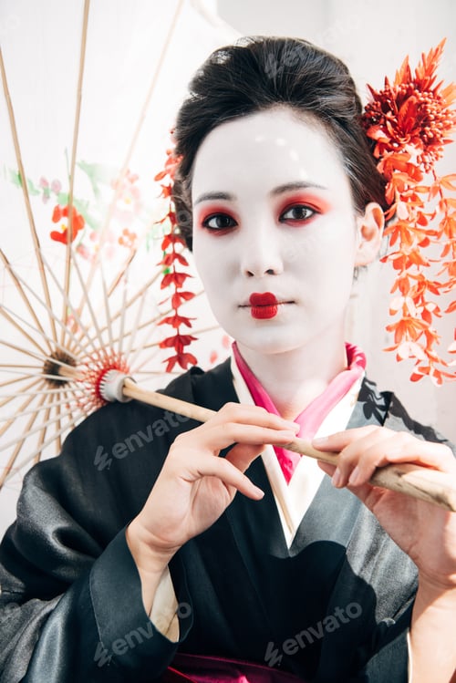 Preview: beautiful geisha with red and white makeup holding umbrella in sunshine