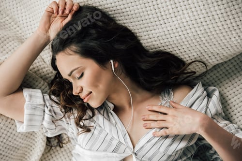 Preview: Beautiful young woman with closed eyes listening music with earphones and smiling