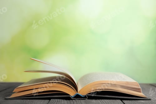 Preview: Open book on blue wooden table against blurred green background. Space for text