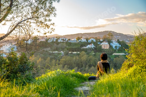 Preview: woman relaxing and meditating at sunset on green hill with beautiful view of countryside and