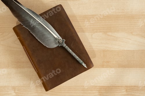Preview: Feather quill pen with old handmade leather notebook, on wooden desk.