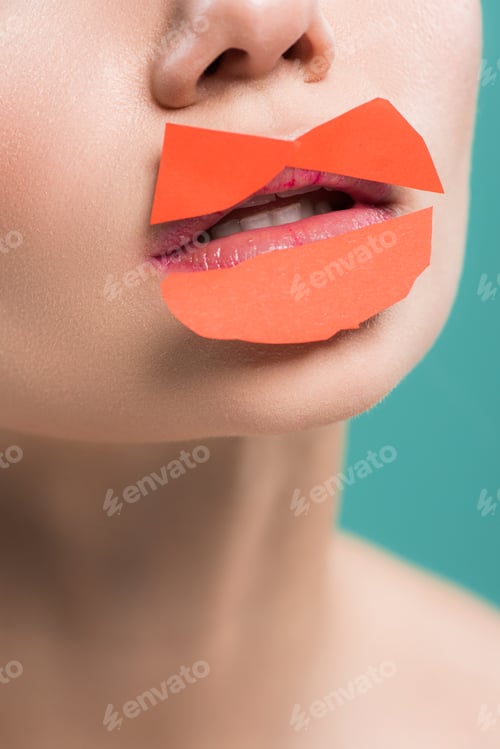 Preview: cropped view of young woman with orange paper on lips isolated on blue
