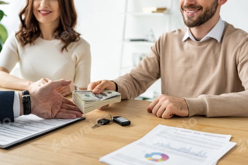 Preview: cropped view of happy man giving dollar banknotes to car dealer near cheerful woman