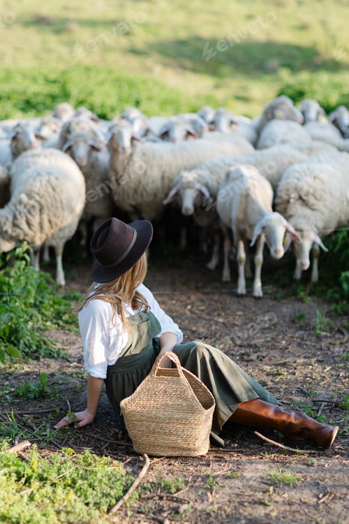 Preview: Young shepherdess sitting and resting near grazing sheep flock