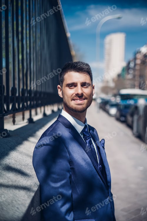 Preview: Smiling young groom near fence on street