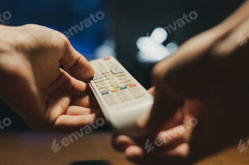 Preview: hands in the dark hold a tv remote and switch channels d