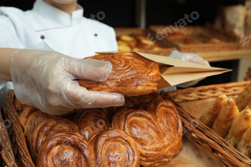 Preview: Baker putting fresh bun into paper bag, closeup