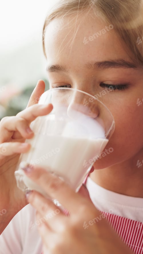 Preview: Girl drinks milk from a glass while sitting indoors during daylight