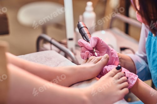 Preview: Young cheerful nail master is working on client's toe nails at her pedicure studio.