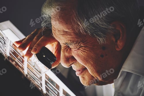 Preview: Senior man looking at sheet of film slides with magnifier