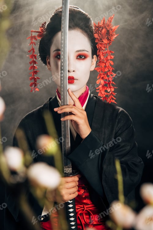 Preview: selective focus of geisha in black kimono holding katana in smoke and sakura branches