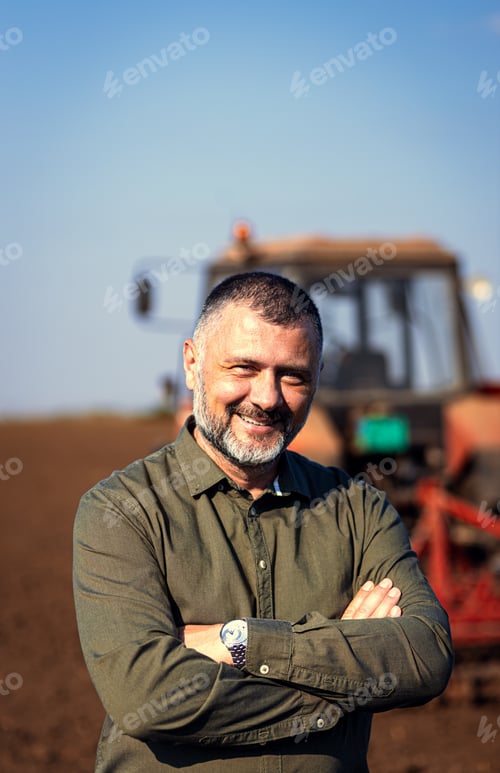 Preview: Portrait of satisfied farmer standing in field preparing to cultivate the land with a tractor.