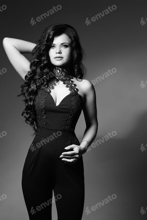 Preview: Studio portrait of sexy brunette woman in black touching curly hair.