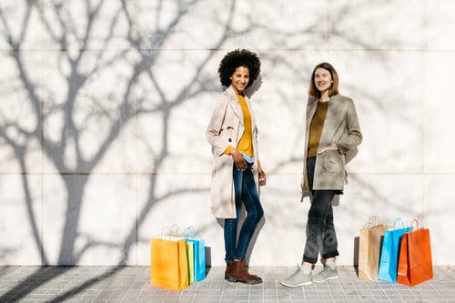 Preview: Portrait of two happy women with shopping bags standing at a wall